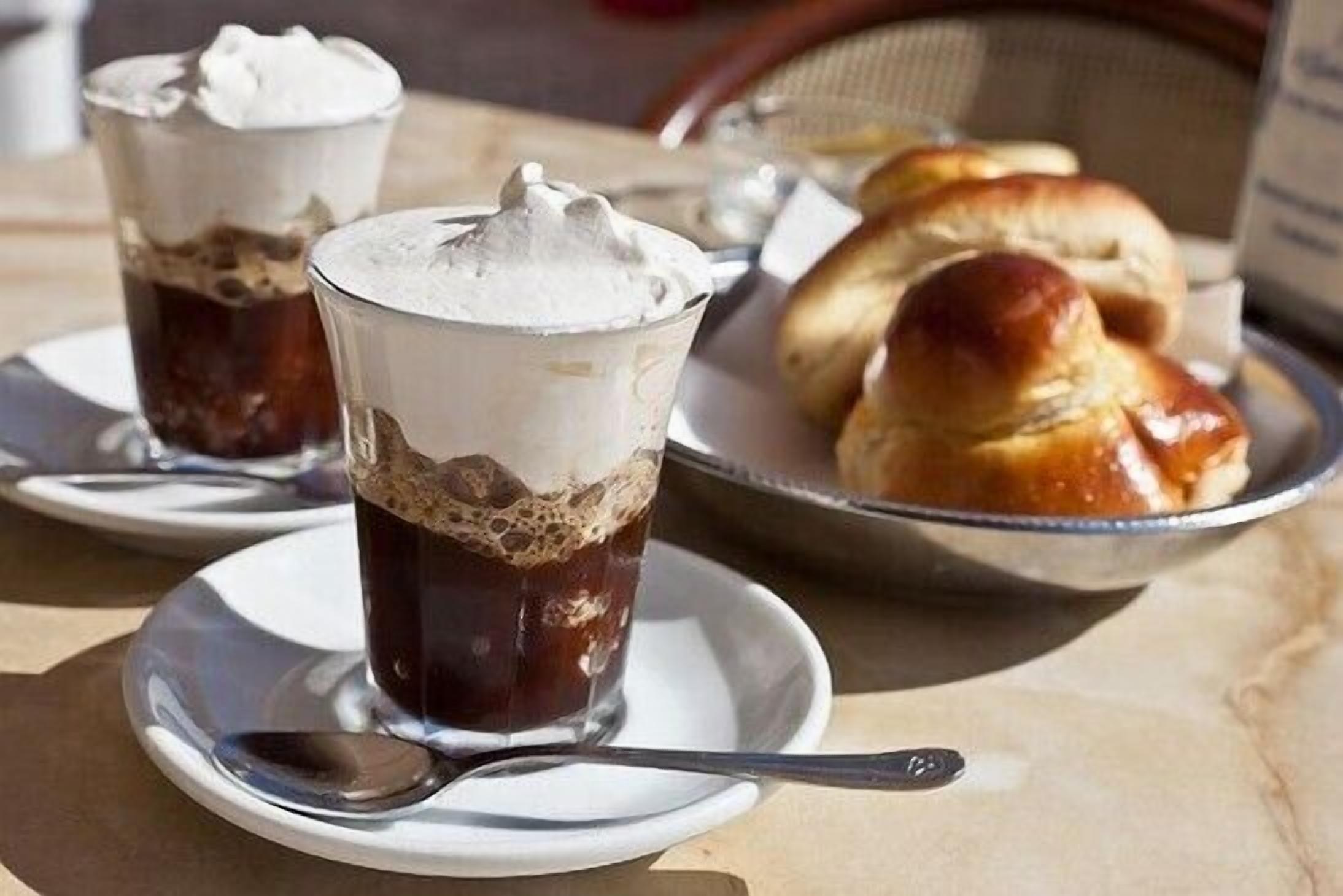 Duas bebidas de café gelado com chantilly sobre uma mesa com uma cesta de pãezinhos.