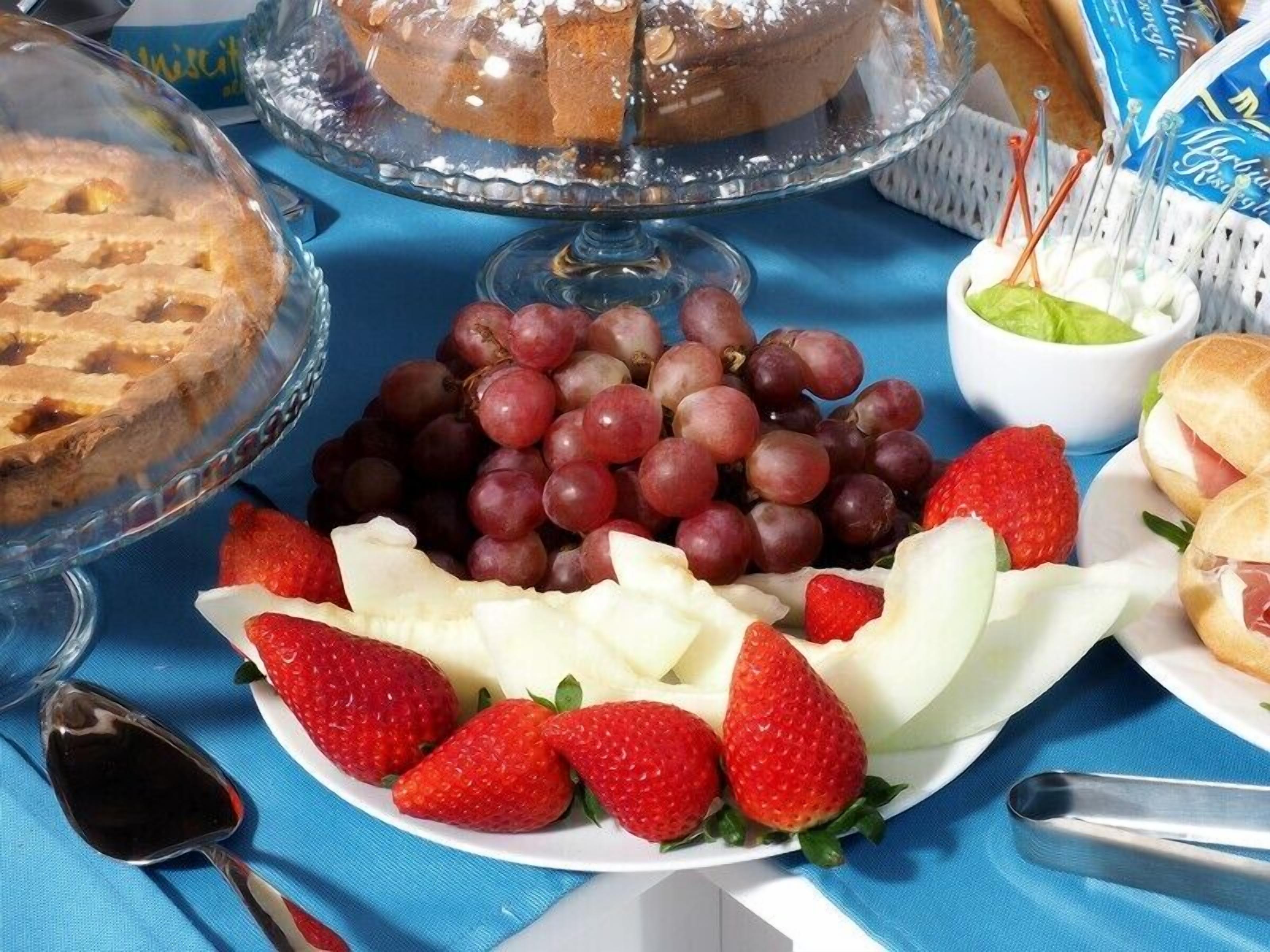 A table with a variety of food items including a pie, grapes, strawberries, and sandwiches.