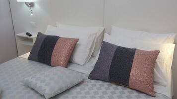 A neatly made bed with patterned bedding and two pillows, a bedside table with a remote control, and a wall-mounted light fixture.