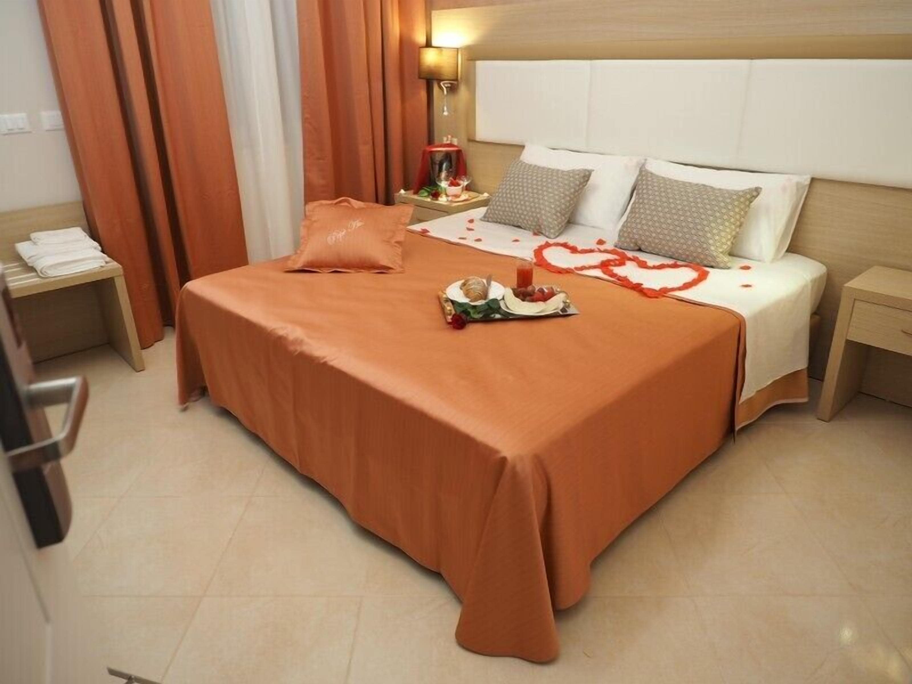Habitación de hotel con una cama bien hecha, una mesita de noche con lámpara y una pequeña mesa con un objeto decorativo.
