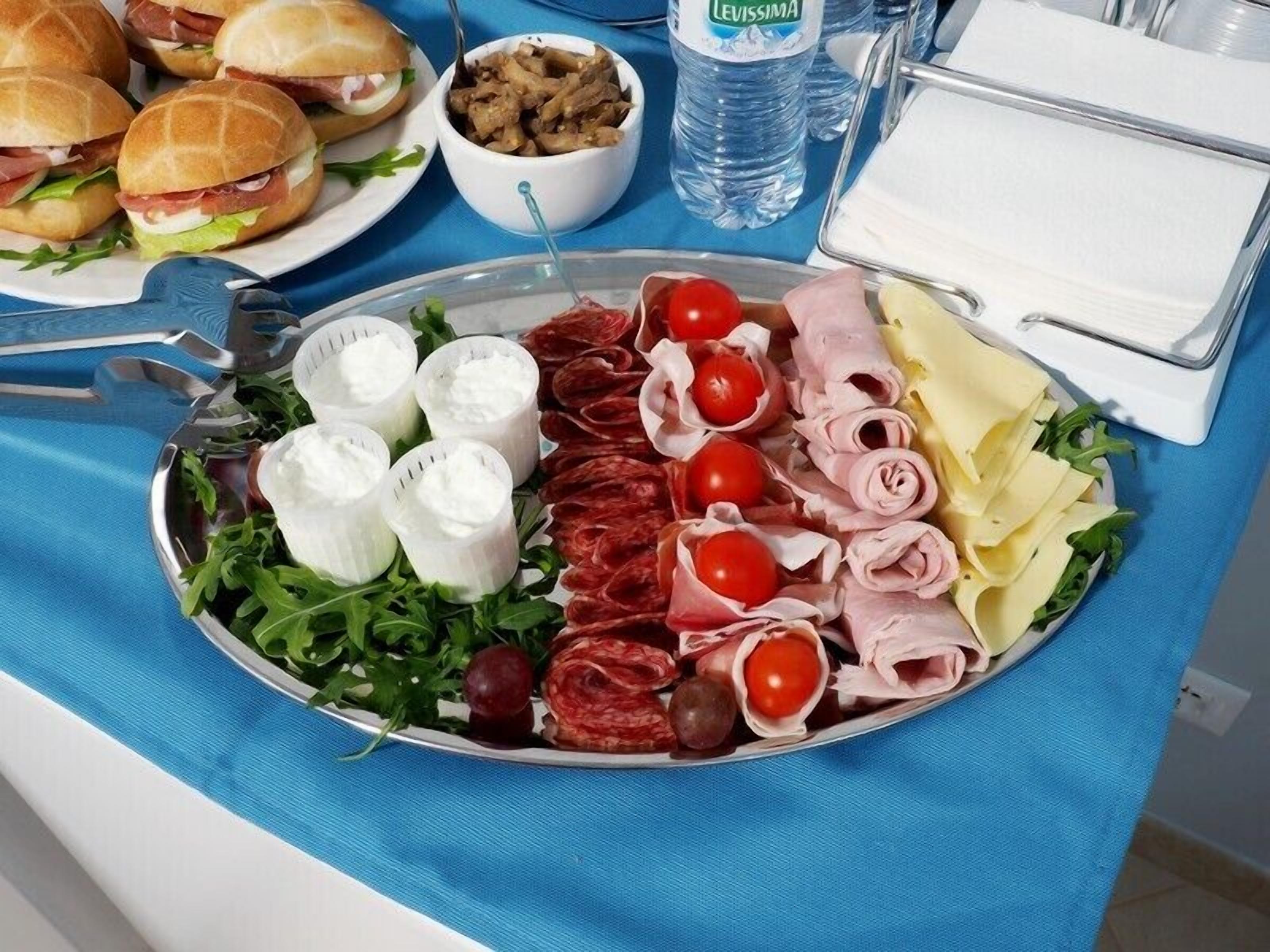 Un tavolo da buffet con diversi tipi di cibo, tra cui panini, insalate e una selezione di formaggi e salumi.