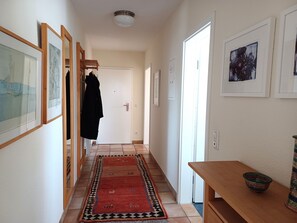 A hallway with framed artwork, a patterned rug, a coat hanging, and a table with a bowl. - At the Bodden Meadows I (Wustrow)