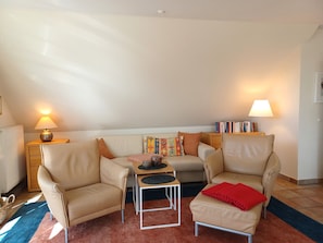 A living room with a sofa, two armchairs, a coffee table, a lamp, a bookshelf, and a radiator. - At the Bodden Meadows I (Wustrow)