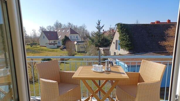 En balkon med fletningsmøbler og et bord, med udsigt over et boligområde med huse og en swimmingpool.