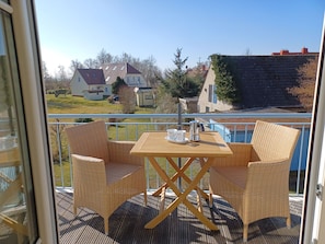 Ein Balkon mit Korbmöbeln und einem Tisch, mit Blick auf ein Wohngebiet mit Häusern und einem Schwimmbad.