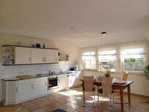 A kitchen with white cabinets, a dining table with chairs, and a window with curtains. - At the Bodden Meadows I (Wustrow)