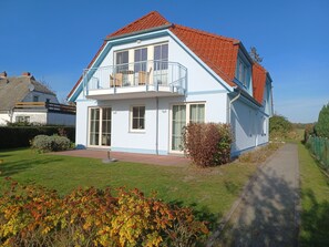 Ein zweistöckiges Haus mit Balkon, rotem Dach und gepflegtem Rasen.