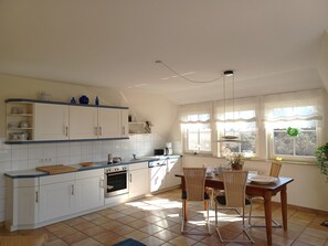 A kitchen with white cabinets, a dining table with chairs, and a window with curtains. - At the Bodden Meadows I (Wustrow)