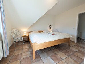 A bedroom with a wooden bed, a nightstand with a lamp, a chair, and a radiator. - At the Bodden Meadows I (Wustrow)