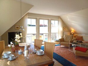 A dining area with a table set for two, a wicker chair, a sofa, and a view of the outside. - At the Bodden Meadows I (Wustrow)