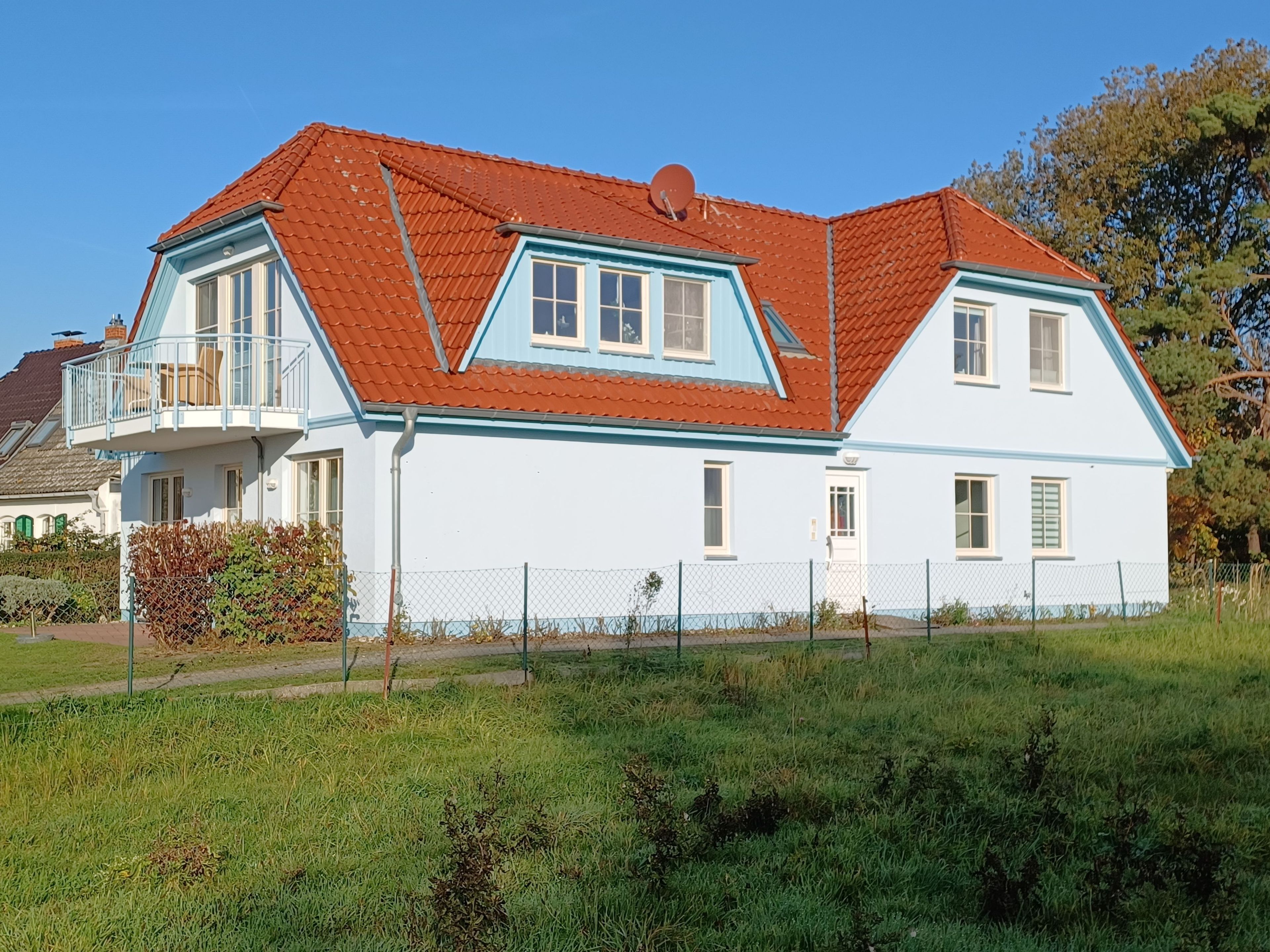 A two-story house with a red-tiled roof, a balcony, and a white exterior.