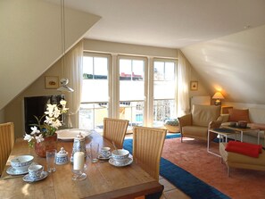 A dining area with a table set for two, a wicker chair, a sofa, and a view of the outside. - At the Bodden Meadows I (Wustrow)