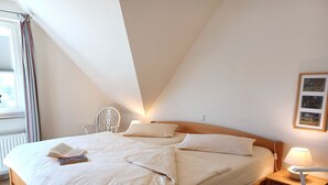 Et soveværelse med seng, natbord, lampe og stol.