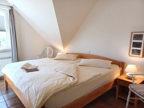 A bedroom with a bed, bedside table, lamp, and a chair. - At the Bodden Meadows I (Wustrow)