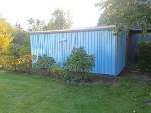 A blue metal shed in a garden with a lawn and trees. - At the Bodden Meadows I (Wustrow)