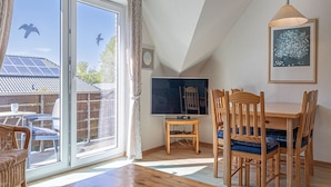 A room with a dining table, chairs, a TV, and a large window with curtains. - Pühler - Apartment Buchfink - FW chaffinch (Kronsgaard)