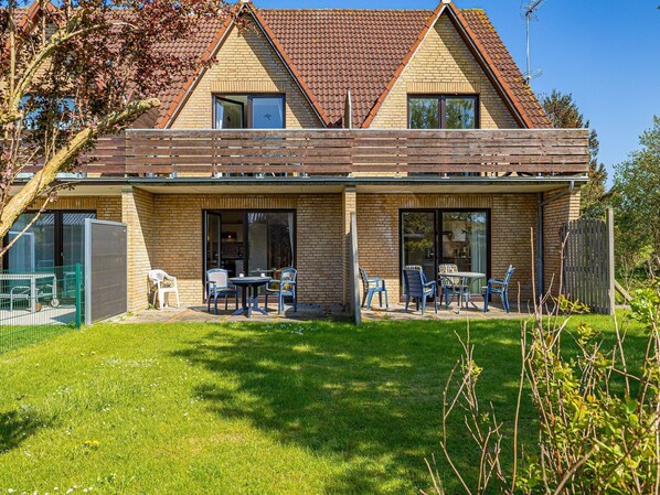 A two-story house with a brick exterior, a tiled roof, and a covered patio area with outdoor seating.