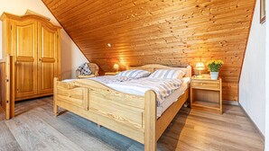 A bedroom with a wooden ceiling, a bed, a nightstand, a chair, and a wardrobe. - Pühler - Apartment Buchfink - FW chaffinch (Kronsgaard)