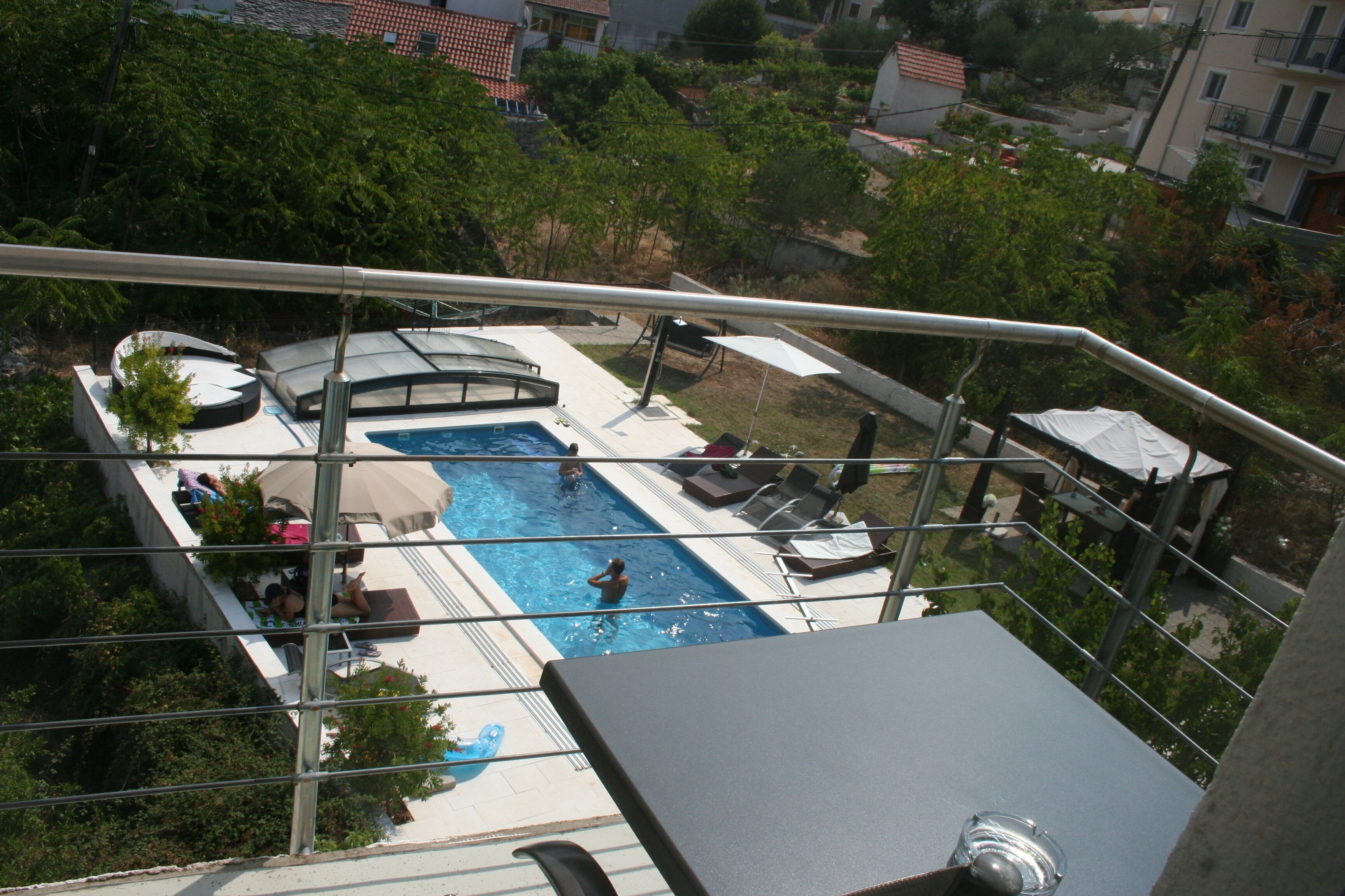 A rooftop pool with lounge chairs and umbrellas, surrounded by greenery and residential buildings.