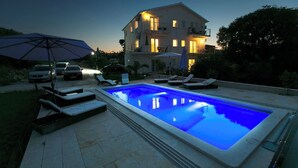 A swimming pool with lounge chairs and umbrellas, surrounded by a paved area and a building with multiple windows and balconies. - Luxury villa with private heated pool and sea view 2 (Marina)