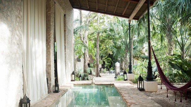 A serene pool area with a clear water surface, surrounded by lush greenery and a covered walkway. - Coqui Coqui Valladolid (Valladolid)