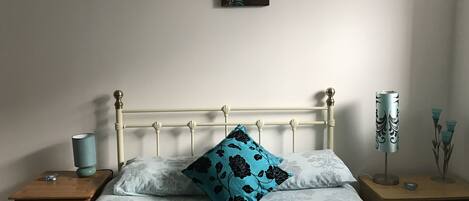 A neatly made bed with a teal and white duvet, a single black and teal pillow, and a small bedside table with a lamp.