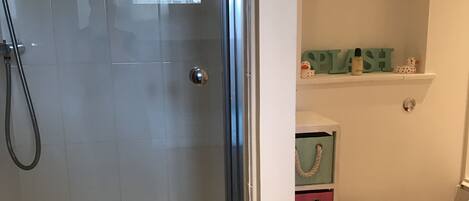 Een badkamer met een glazen douchedeur, een toilet, een plankje met decoratieve spullen en een klok aan de muur.