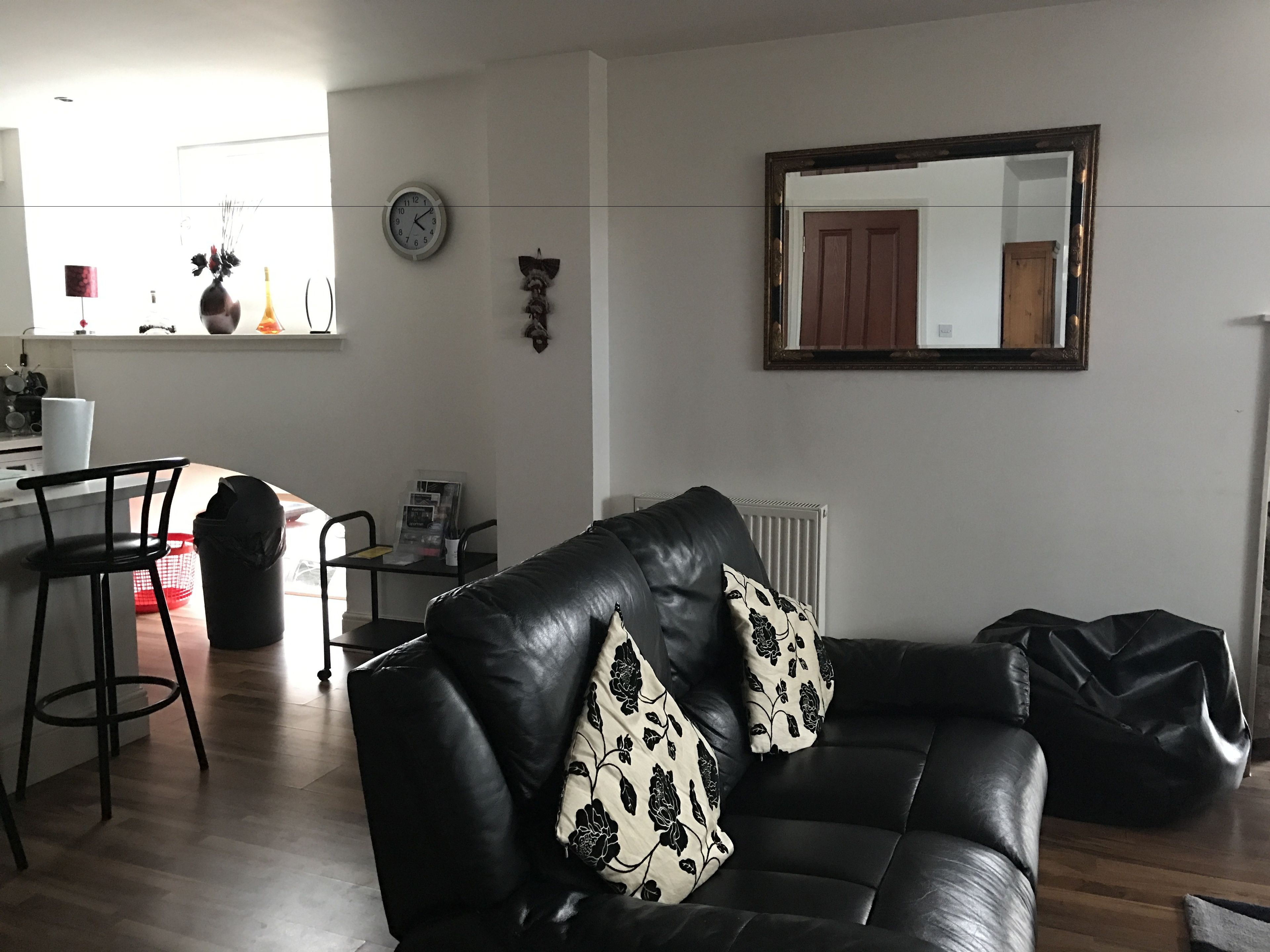 A living room with a black leather sofa, a red chair, a small table with a newspaper, and a radiator.