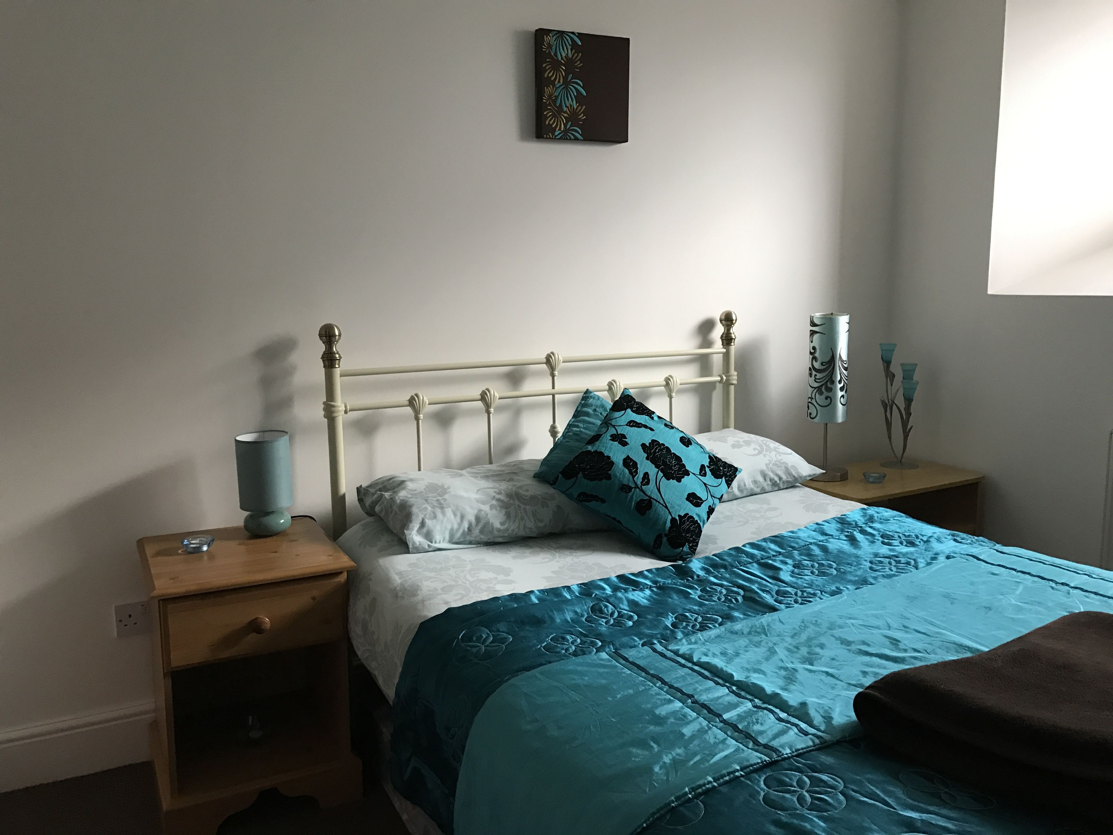 Quarto com cama, mesas de cabeceira, abajur e uma obra de arte na parede.