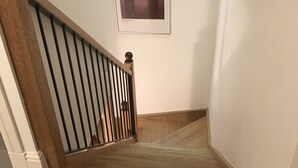 Un escalier avec des marches en bois et une rampe en métal, menant à un palier où est accrochée une image encadrée au mur.