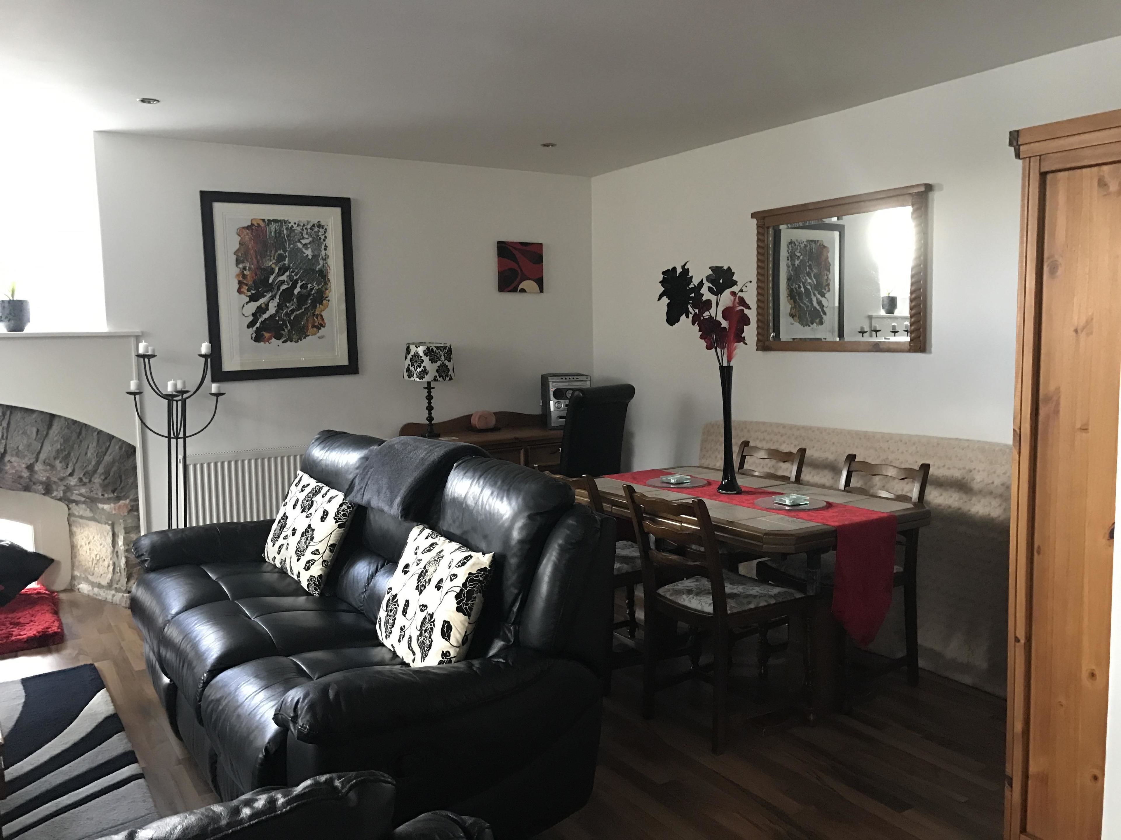 A living room with a black leather sofa, a dining table with chairs, a fireplace, and framed artwork on the walls.