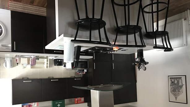Une cuisine moderne avec des meubles noirs, un îlot central en acier inoxydable et des luminaires suspendus.