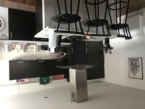 Une cuisine moderne avec des meubles noirs, un îlot central en acier inoxydable et des luminaires suspendus.