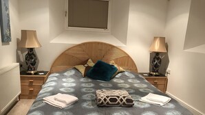 Une chambre à coucher avec un lit, deux tables de chevet, une fenêtre et un radiateur.