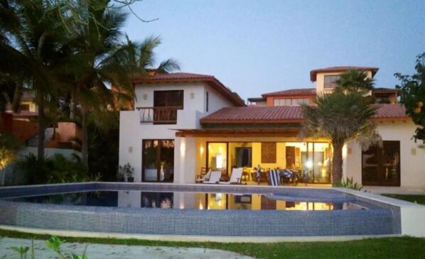 Une maison à deux étages avec une piscine en premier plan.