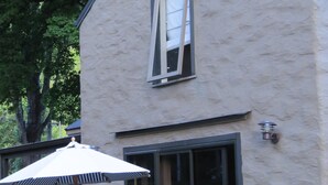 Un edificio de dos pisos con un amplio ventanal corredero, un patio con mesa y sillas, y una cerca de madera.