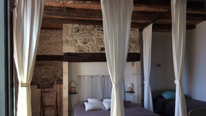 A bedroom with a stone wall, wooden beams, a bed with a canopy, a bedside table with a lamp, and a small shelf with a decorative item. - Character house in Montignac Lascaux (Montignac)