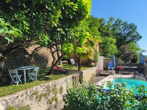 A pool area with a stone wall, lounge chairs, and umbrellas.