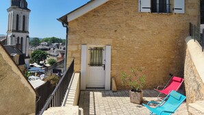 A stone building with a white door, a balcony with blue chairs, and a view of a tower in the background. - Character house in Montignac Lascaux (Montignac)