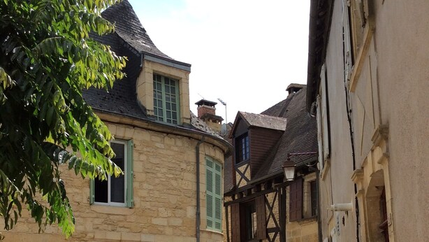 A narrow cobblestone street between old stone buildings with traditional architecture, including timber framing and green shutters. - Character house in Montignac Lascaux (Montignac)