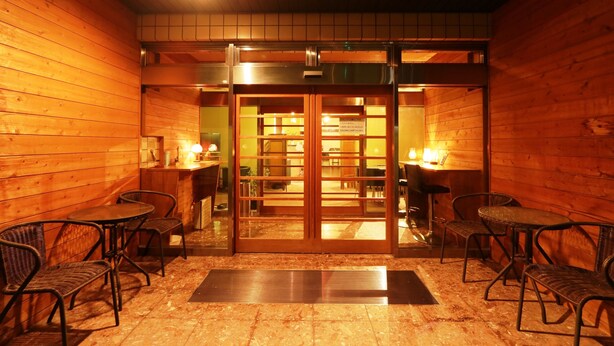 A wooden interior with a sliding glass door leading to a dining area. There are four tables and chairs arranged around the room. - HOTEL Rakuserina (Fuefuki)
