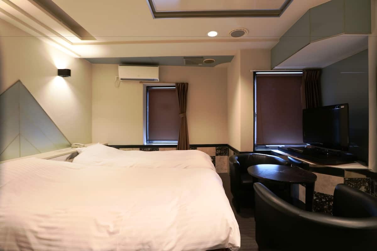 A hotel room with a bed, a desk, a chair, a TV, and a window with curtains.