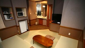 A compact hotel room with a kitchenette, a flat-screen TV, a wooden bench, and a small seating area. - HOTEL Rakuserina (Fuefuki)