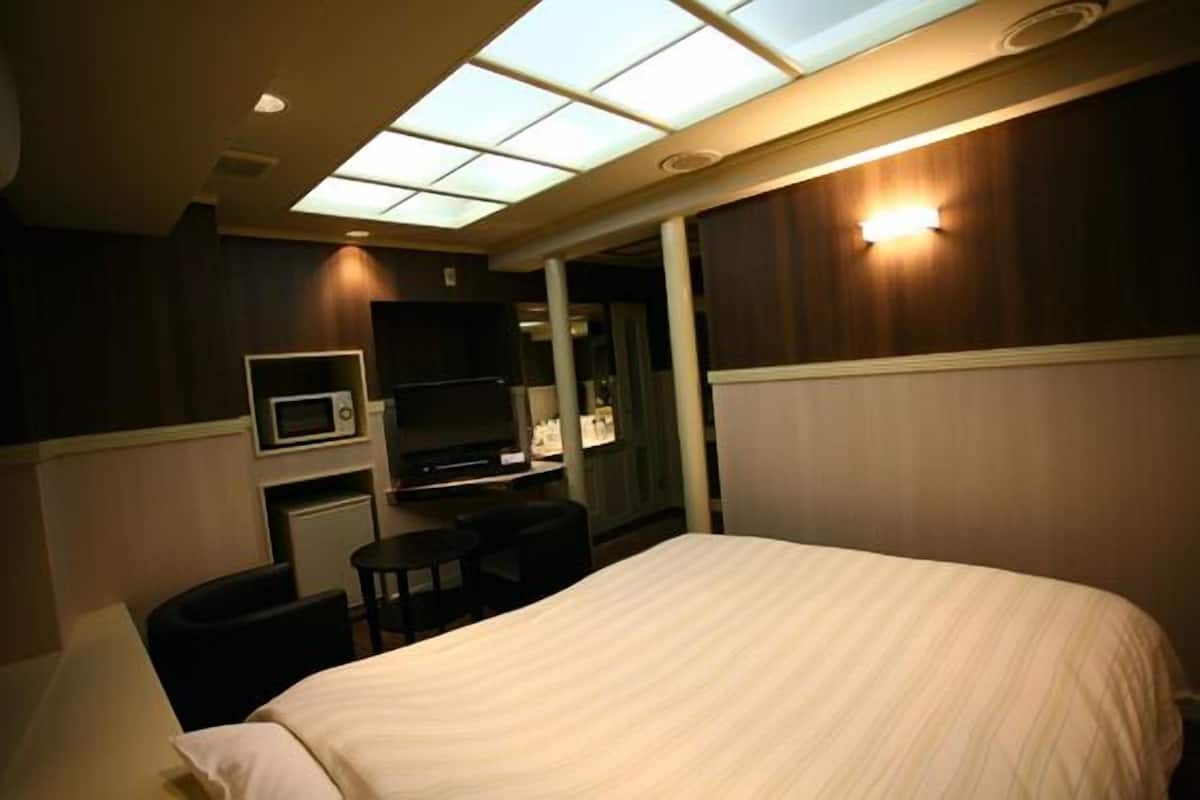 A hotel room with a bed, a desk with a computer, a microwave, and a television.