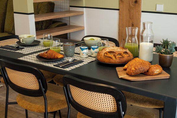 A breakfast table set with croissants, a loaf of bread, and various beverages.