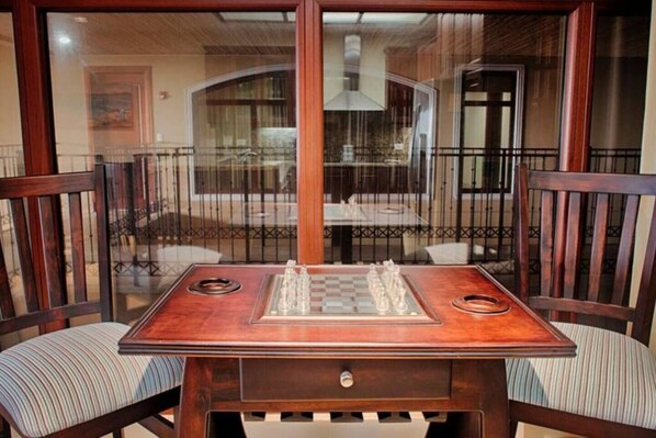 A wooden chess table with two chairs, a small drawer, and a glass top.