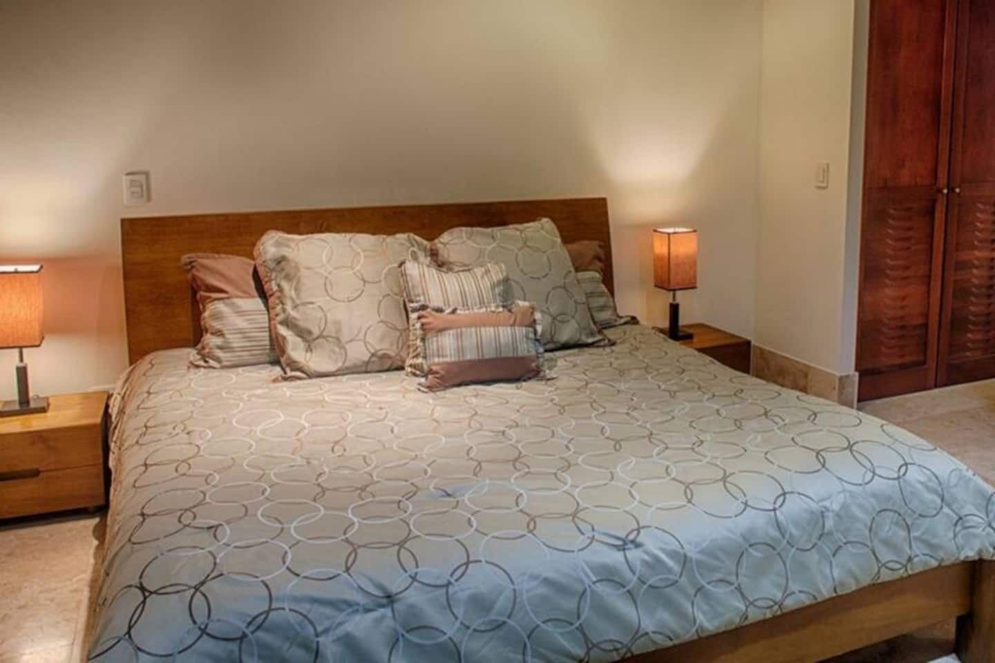 A neatly made bed with a patterned bedspread, two bedside lamps, and a wooden headboard.