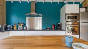 Eine Küche mit türkisfarbenen Wänden, einer Holz Arbeitsplatte und Edelstahlgeräten, darunter ein Backofen und eine Kaffeemaschine.