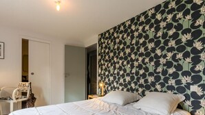 Ein Schlafzimmer mit einem Bett, weißer Bettwäsche, einem Sessel und einer Wand mit floralem Muster.