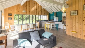 Ein geräumiges Loft mit hohen Decken, freiliegenden Holzbalken, einer Küche mit Kochinsel und großen Fenstern mit Blick ins Freie.
